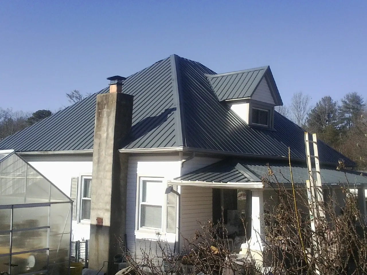 Dark blue standing seam metal roof on a white farmhouse with dormer — Slate & Tile Roof Repair by Roofing Brothers in Fort Collins