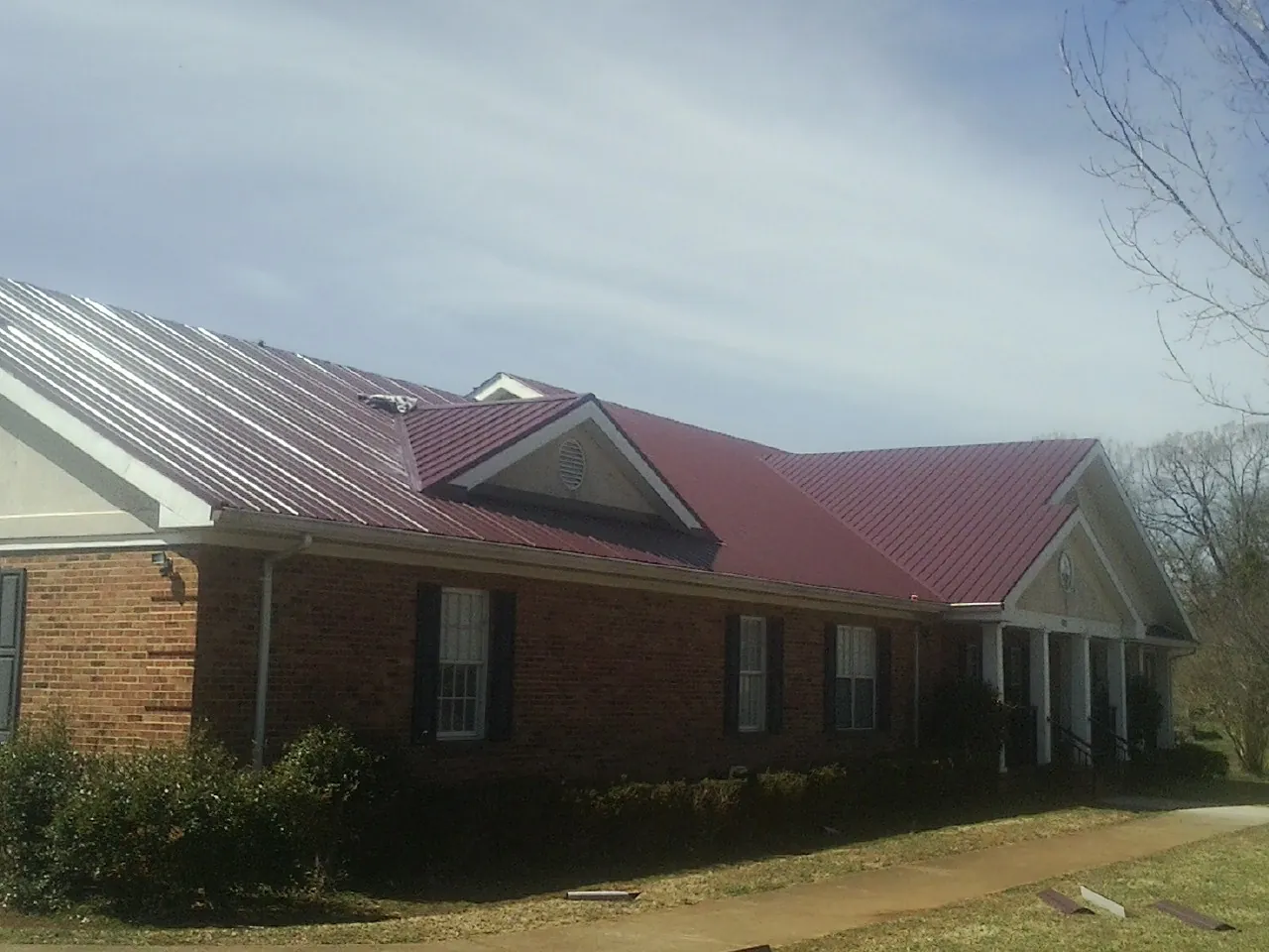 Red metal roof with gabled entries on a long brick building, from a Hail Damage Roof Repair job in Fort Collins