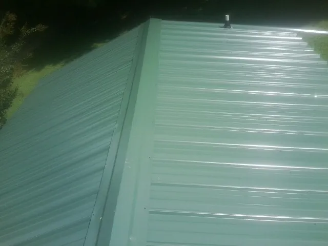 New green metal panels meeting at the ridge of a roof — Flat Roof Repair work by our crew in Fort Collins