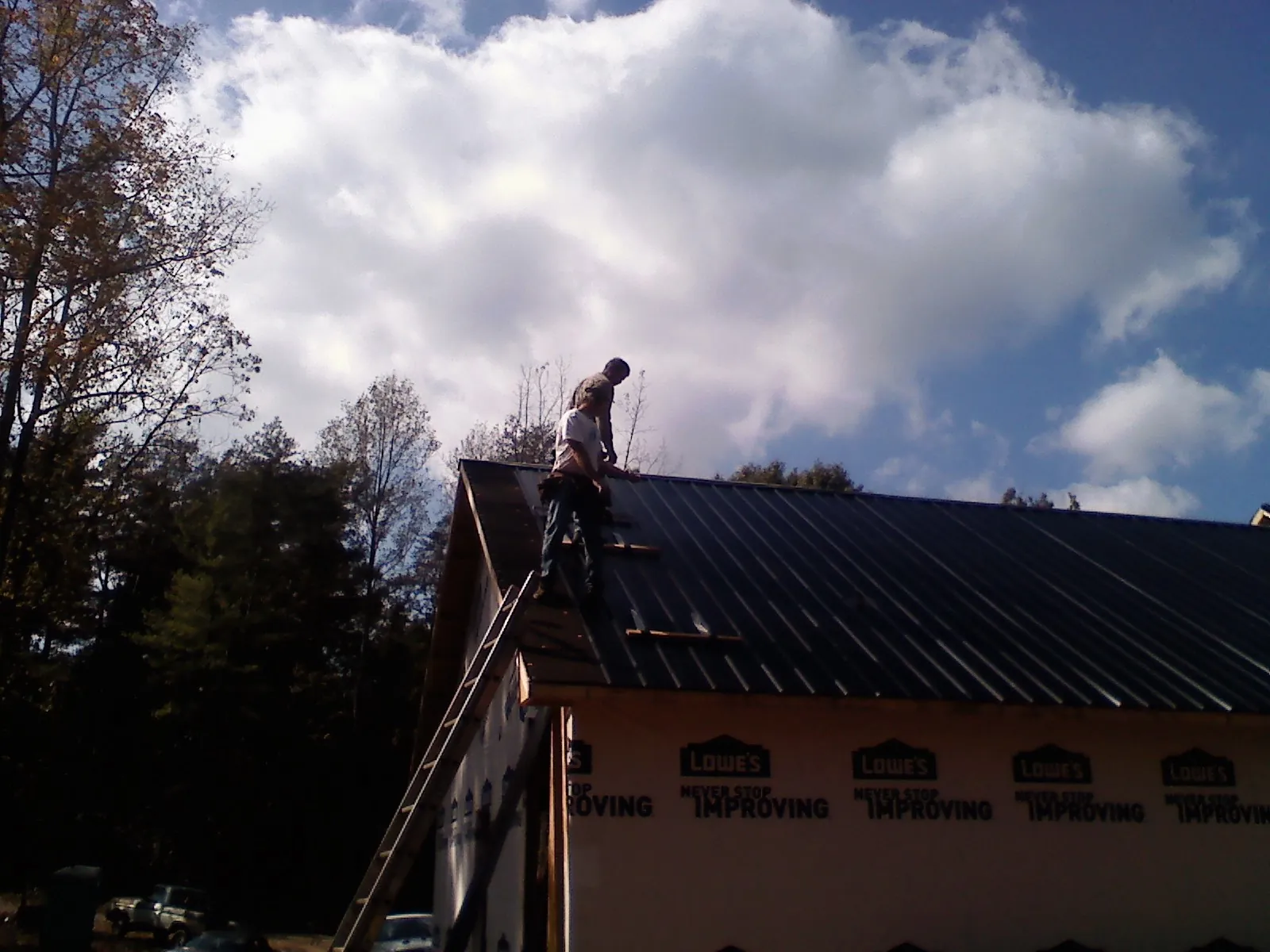 Roofer fastening dark metal panels high against a cloudy sky, from a Roof Inspection job in Fort Collins