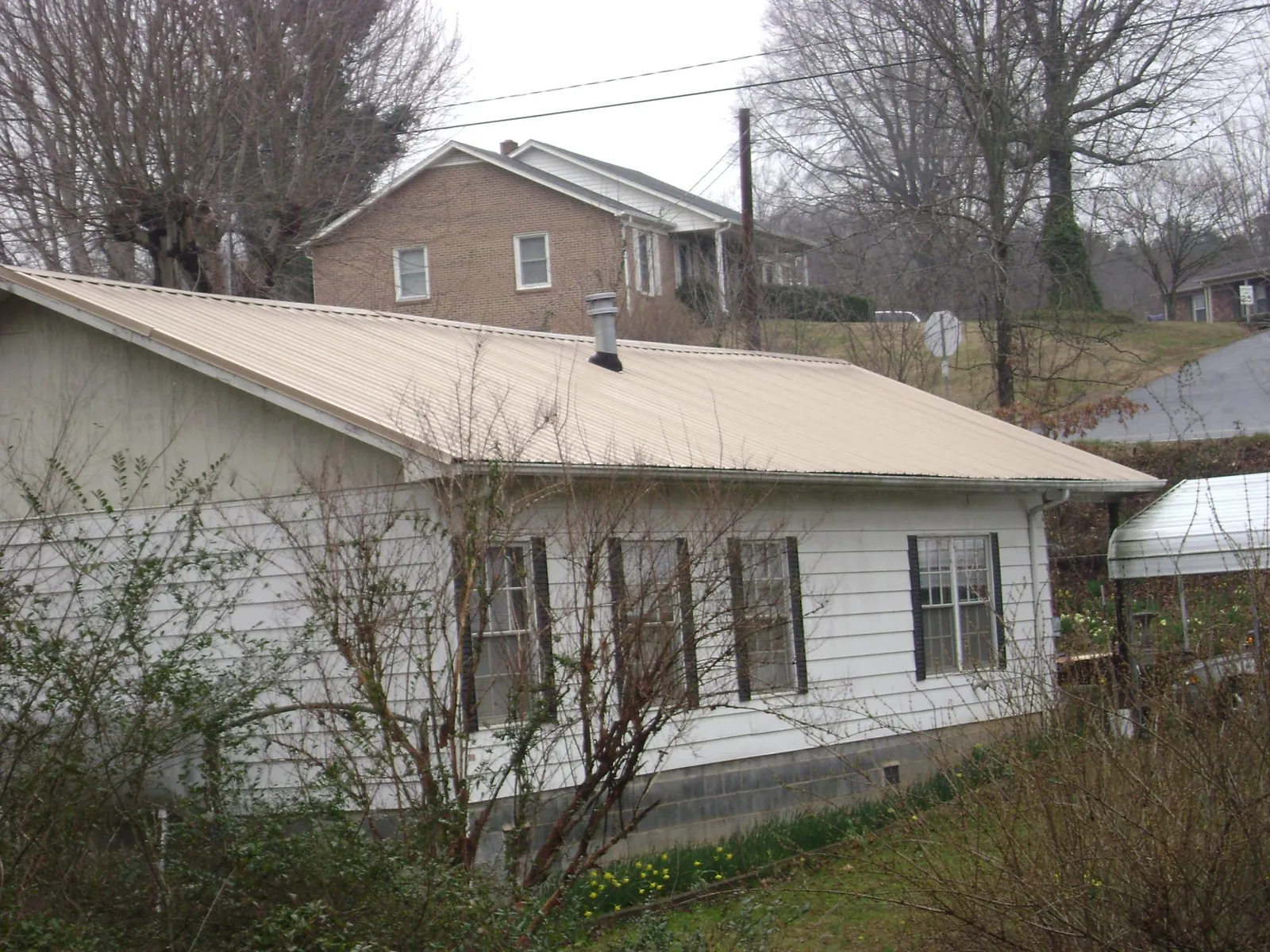 Tan metal roof on a white sided house set into a hillside — Commercial Roofing by Roofing Brothers in Fort Collins