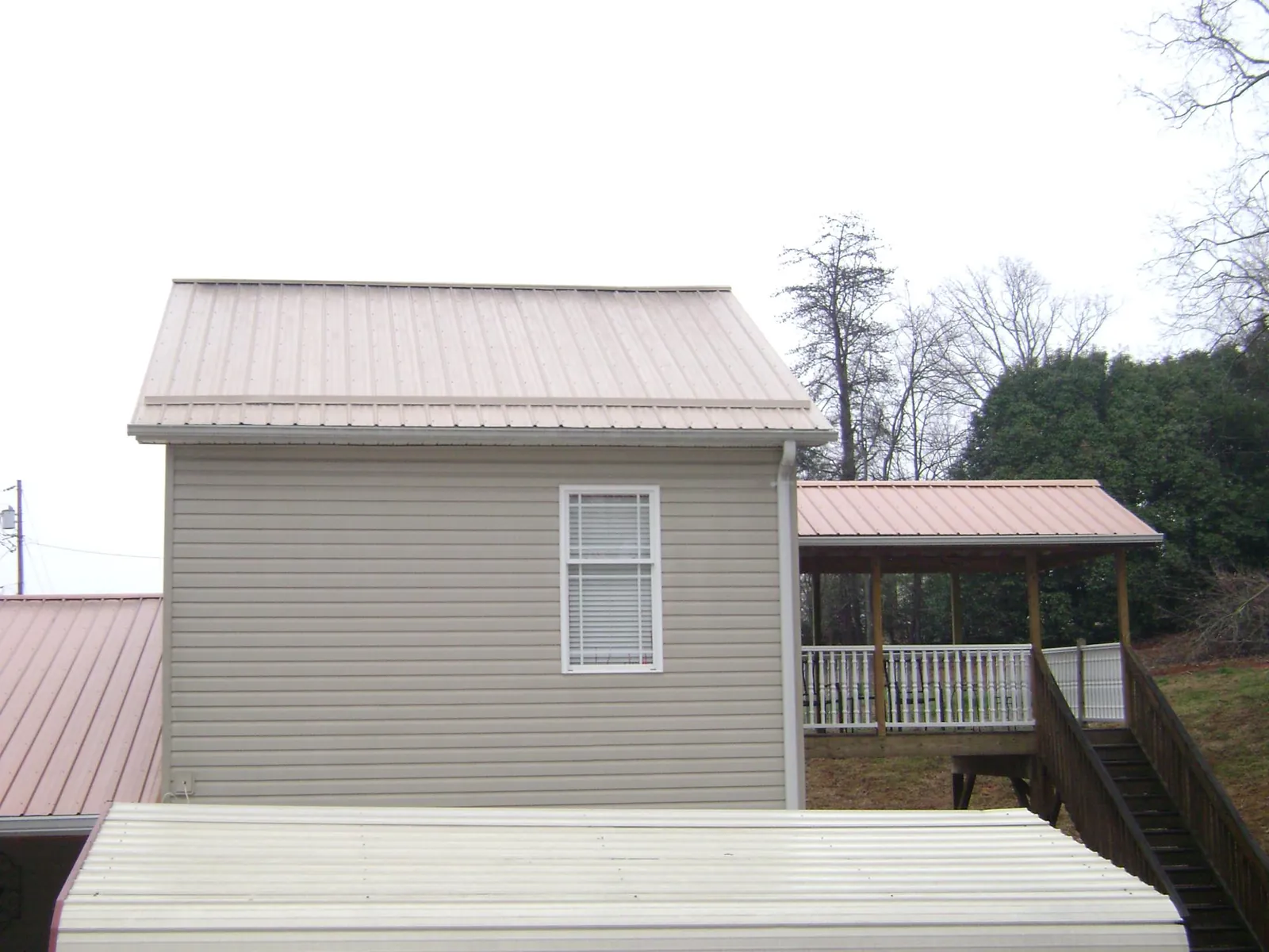Tan metal roofs on a two story addition and attached porch, from a Roof Replacement job in Fort Collins